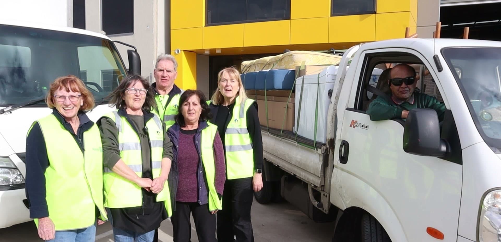 Five WERN volunteers in high-visibility vests standing with the WERN truck outside the Ravenhall warehouse.